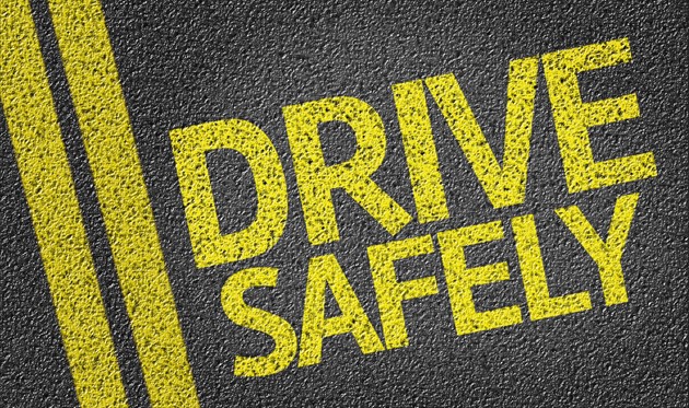 Text on asphalt reads "DRIVE SAFELY" in large yellow letters with yellow lines parallel to the left side. The texture resembles a road surface.