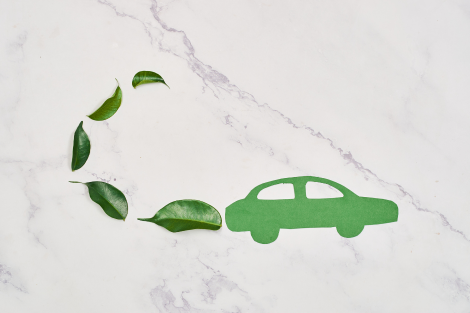 A green paper cutout of a car rests on white marble, with green leaves behind it like exhaust smoke, symbolizing eco-friendly vehicles and the safety benefits of eco-driving.